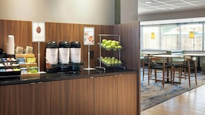 A hotel reception area with a coffee station, fresh fruit display, and seating area.