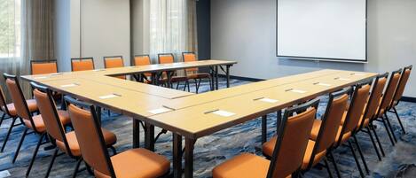 A conference room with a long table, orange chairs, a projector screen, and a carpeted floor.