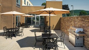 An outdoor patio with tables and chairs, umbrellas, and a barbecue grill.