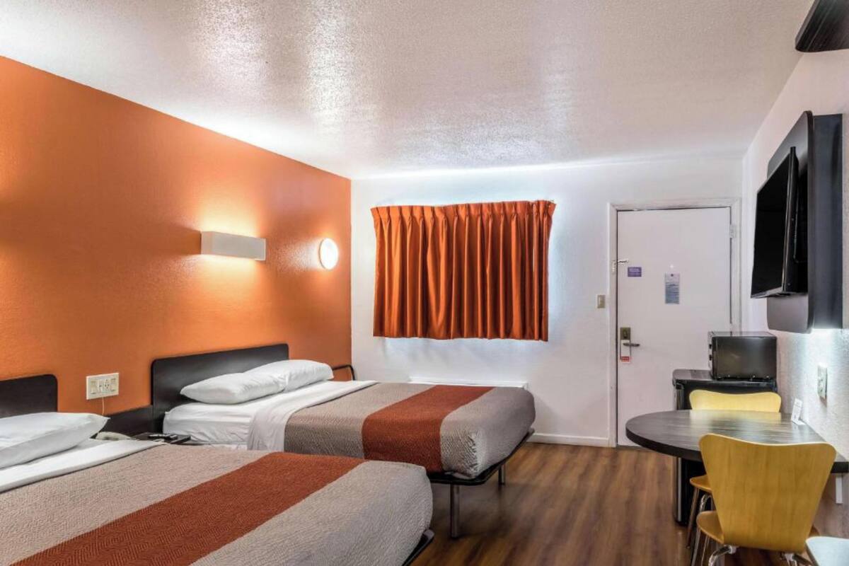 A hotel room with two beds, a desk, a chair, a TV, and a window with curtains.