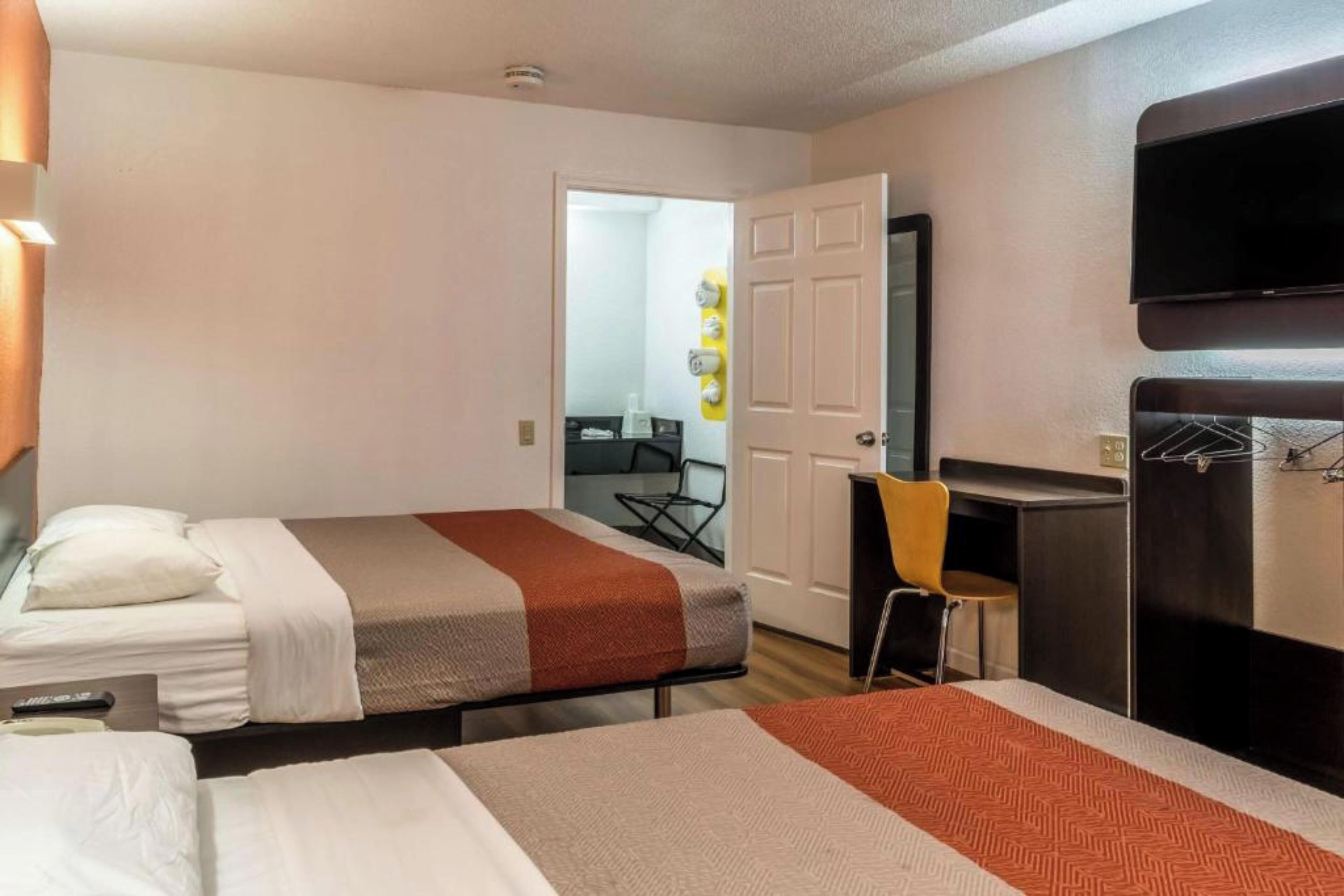 Een hotelkamer met twee bedden, een bureau, een stoel en een aan de muur bevestigde televisie.
