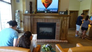 A living room with a fireplace, a television mounted above it, and a small table with a vase of flowers.