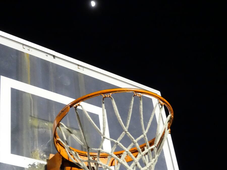 Ein Basketballkorb mit Netz vor einem Gebäude mit großen Fenstern.