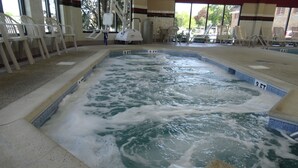 A hot tub with a tiled edge and a view of the outdoors through large windows.
