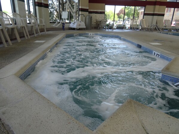 A hot tub with a tiled edge and a view of the outdoors through large windows.
