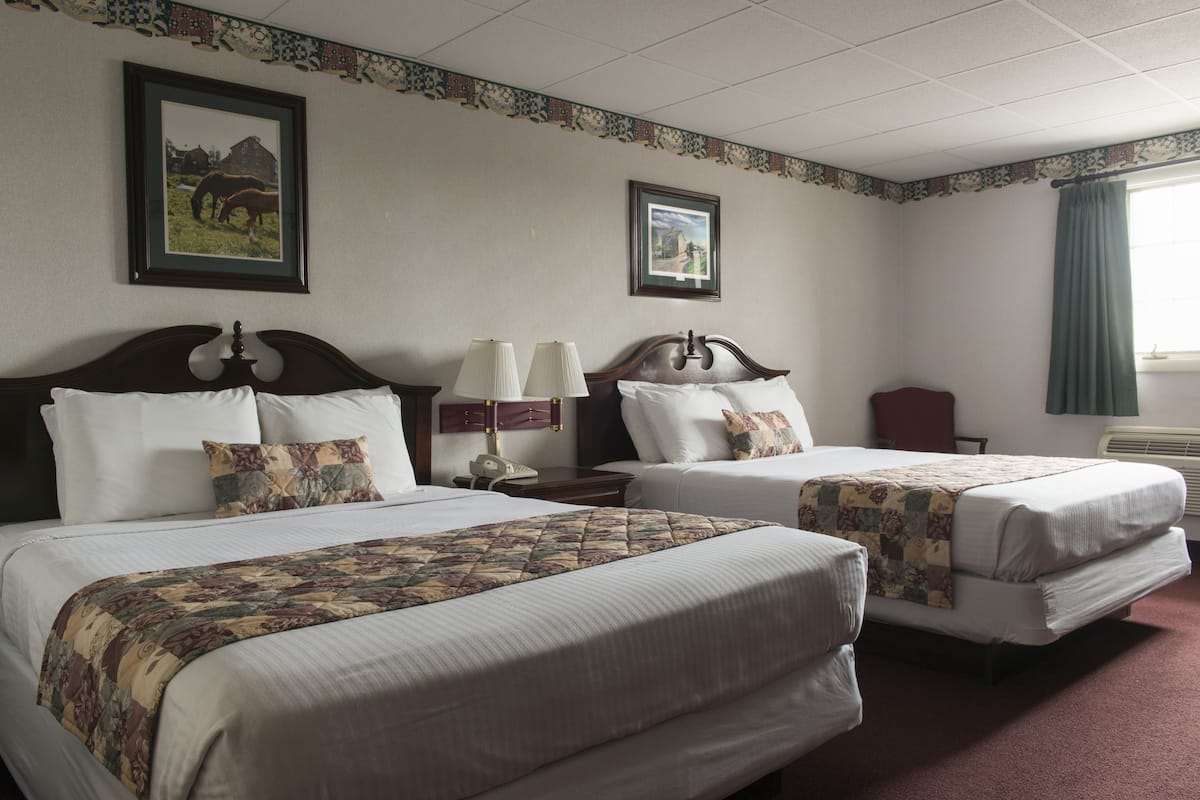 A hotel room with two beds, a nightstand, a lamp, and a window with curtains.