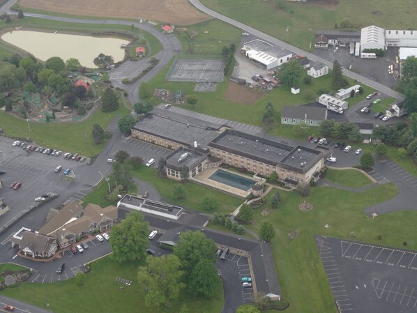 An aerial view of a large building complex with multiple parking areas, a swimming pool, and surrounding greenery. - Bird in Hand Family Inn (Bird In Hand)