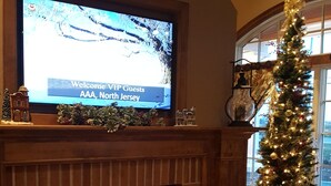 A fireplace with a TV mounted above it displaying a welcome message. A Christmas tree is visible in the background.