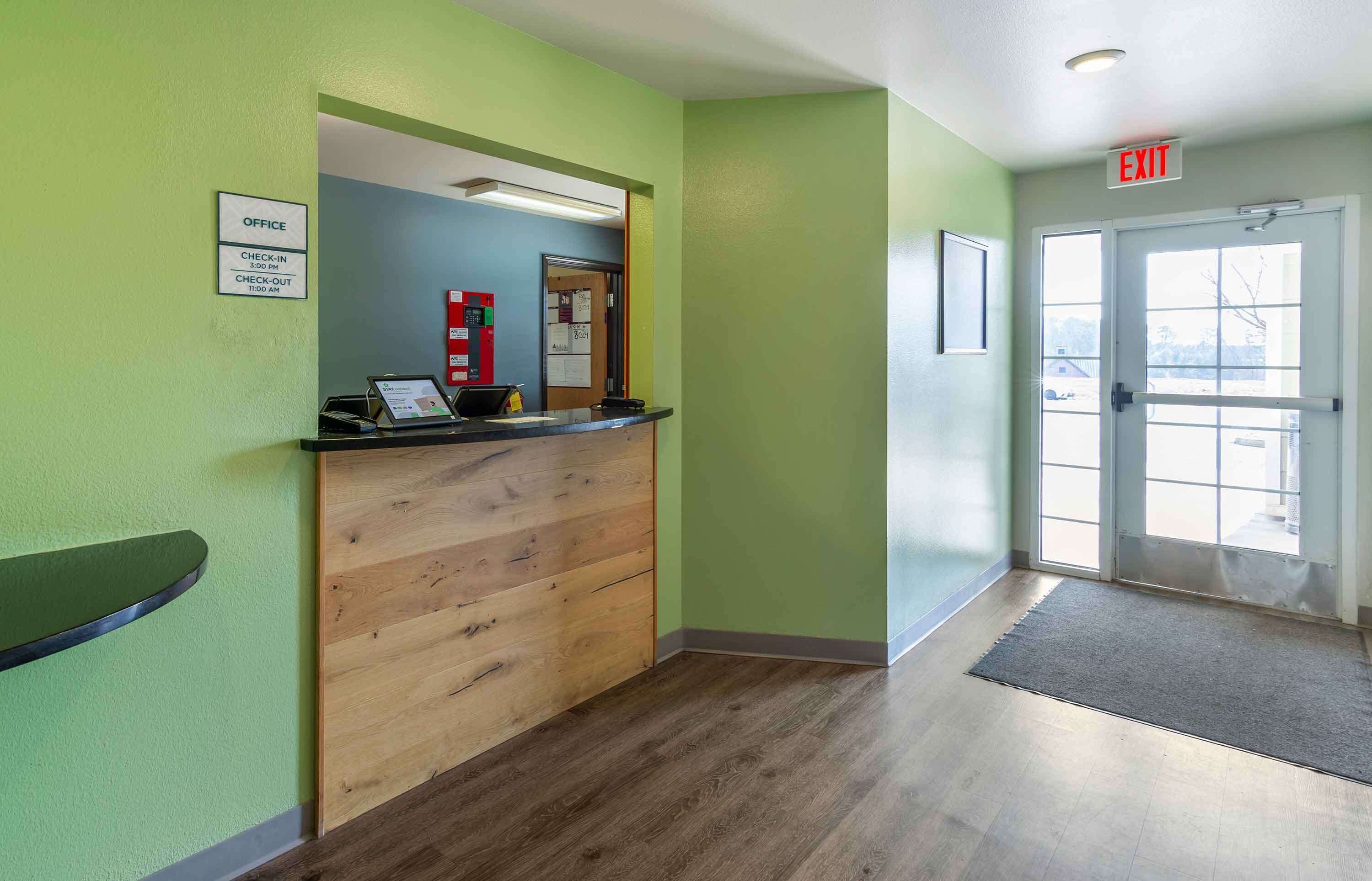 A reception area with a wooden desk, a sign indicating office hours, and an exit sign.