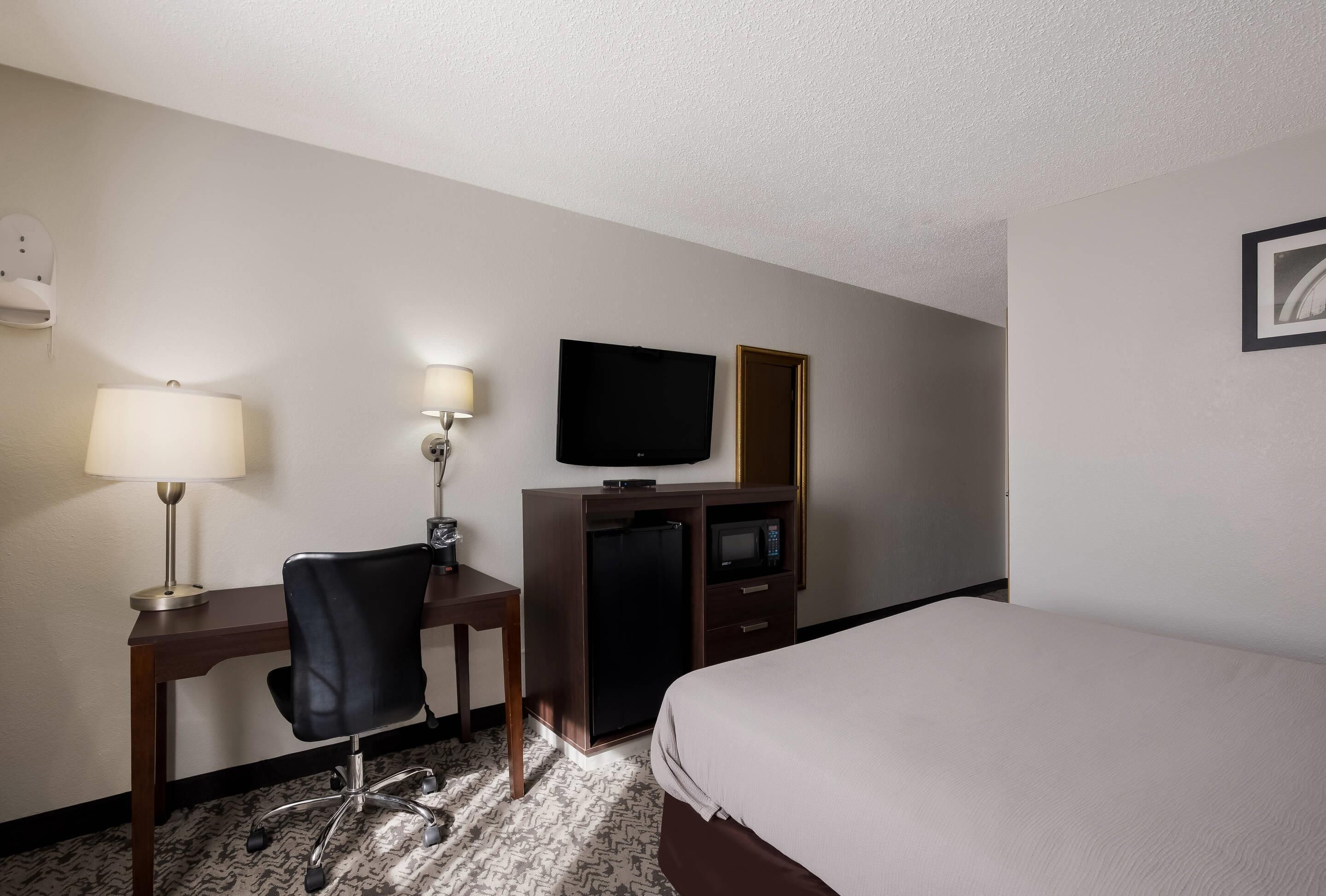 Habitación de hotel con cama, escritorio con silla, televisión, microondas y refrigerador pequeño.