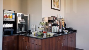 A coffee station with multiple coffee machines, a refrigerated display case, and various coffee cups and mugs. - Quality Inn Hall of Fame (Canton)