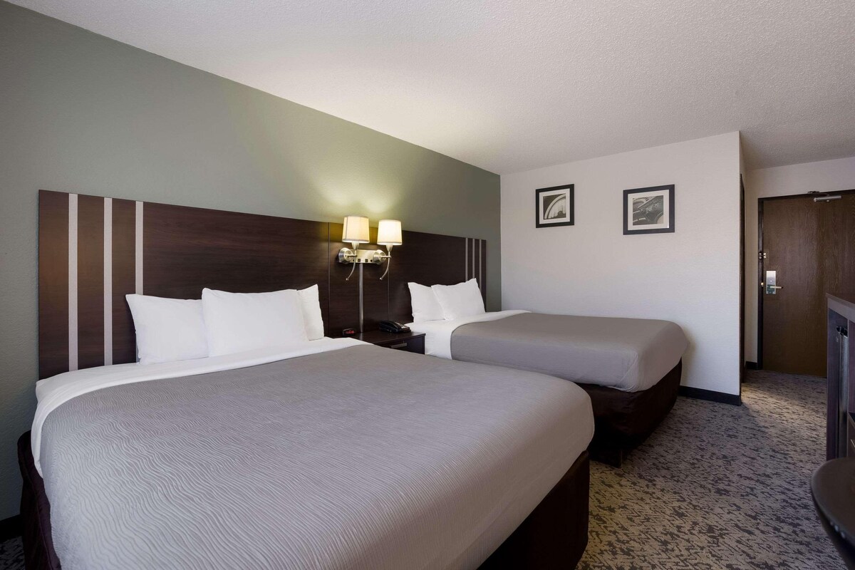 A hotel room with two beds, a nightstand with lamps, and a door.
