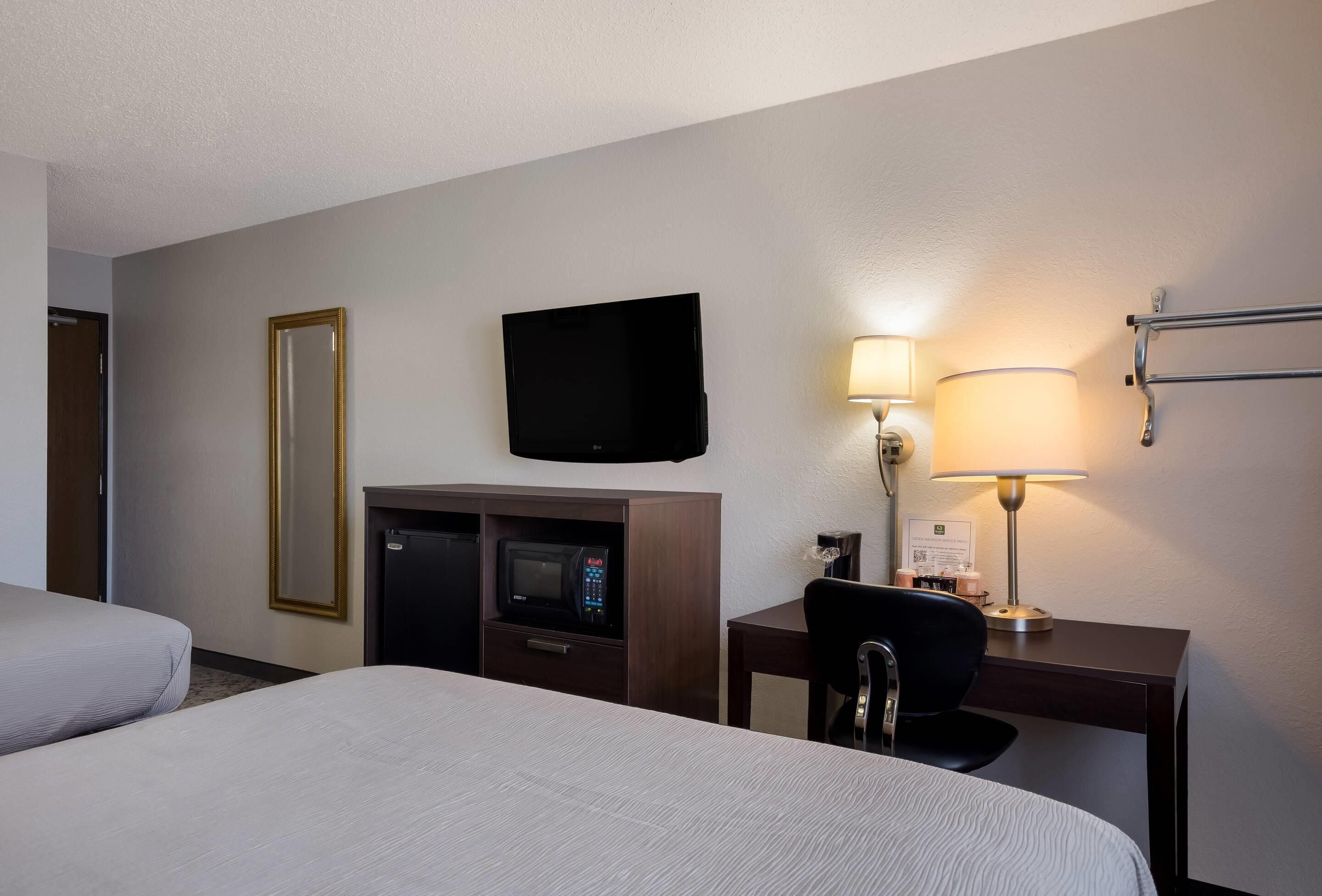A hotel room with two beds, a flat-screen TV, a desk with a lamp, a chair, and a minibar.