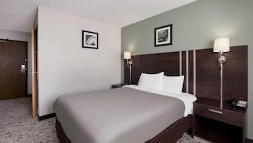 A hotel room with a large bed, two bedside tables with lamps, a wooden headboard, and two framed pictures on the wall.