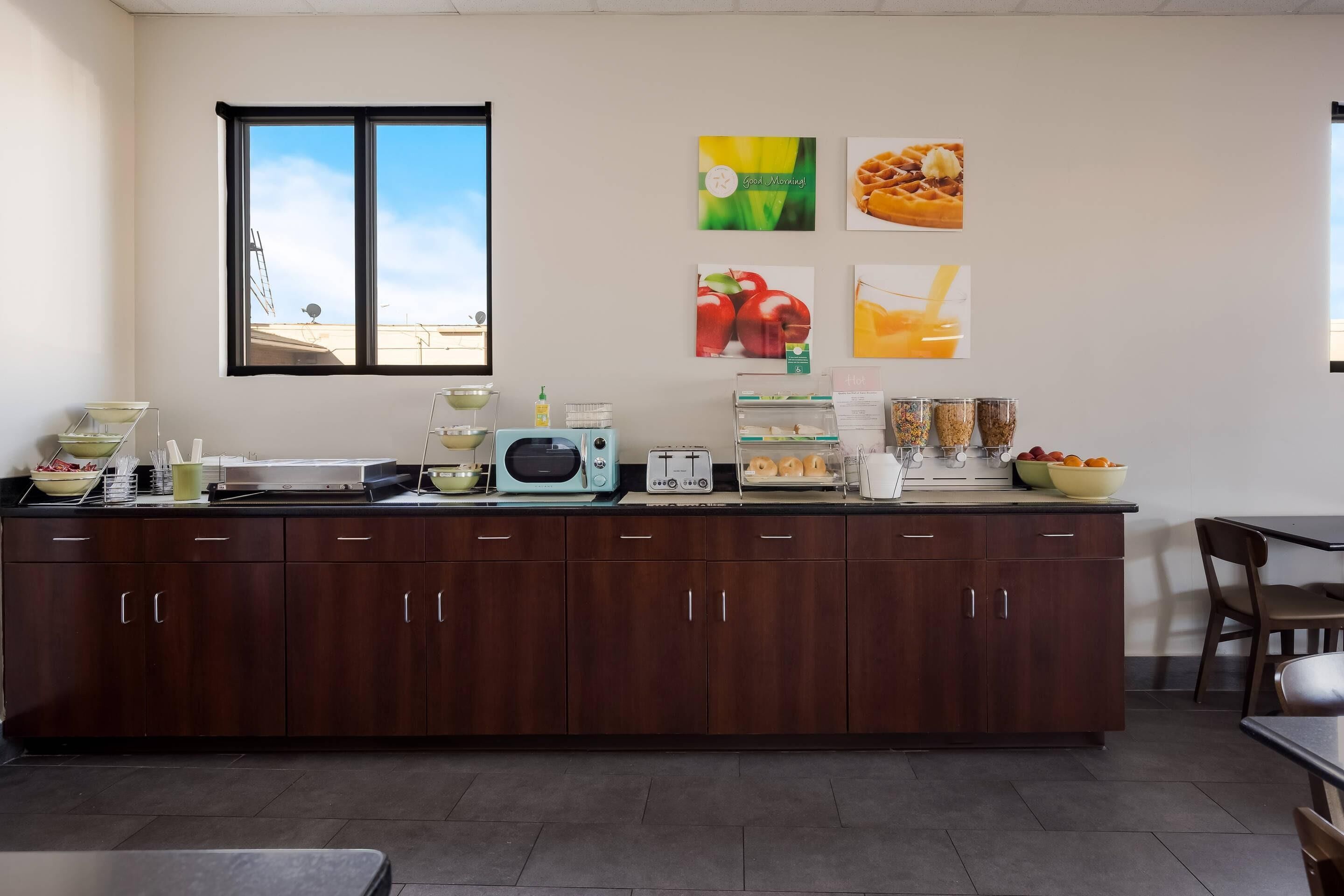 A kitchen with a large window, wooden cabinets, a microwave, toaster, and various food items on the counter.