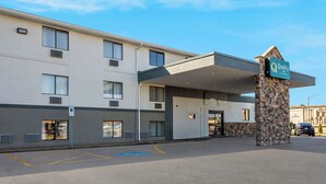 A hotel entrance with a covered walkway, a stone pillar with a sign, and a parking lot with handicapped parking spaces. - Quality Inn Hall of Fame (Canton)