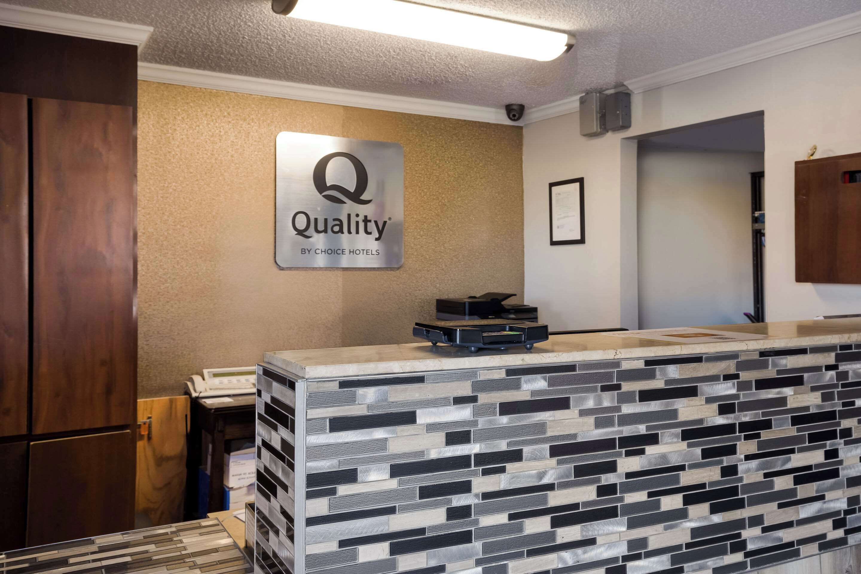 Een hotel receptie met een modern design, een bord met de tekst 'Quality by Choice Hotels' en een receptiebalie met een betegelde spatwand.