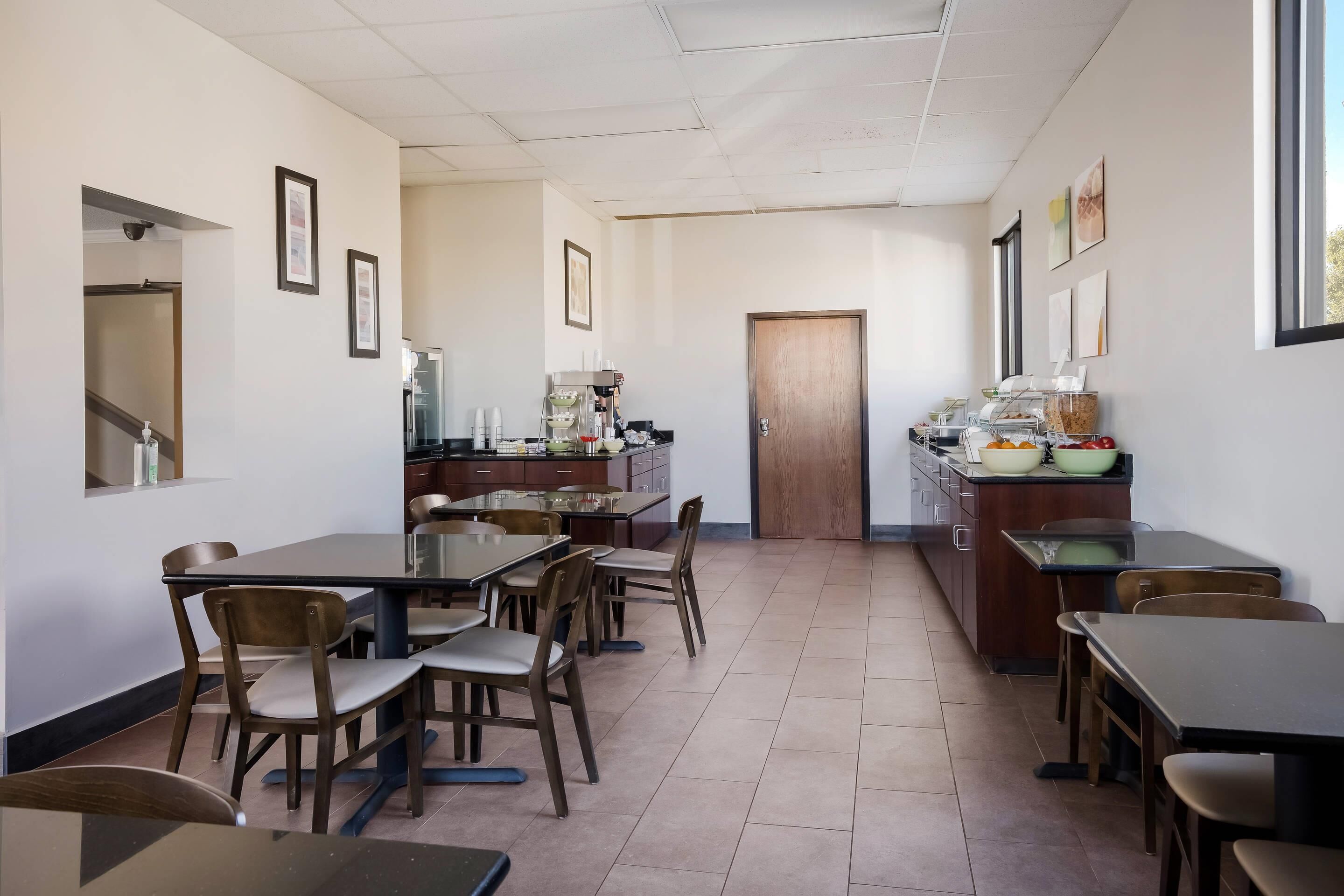 A dining area with tables and chairs, a kitchen area with appliances, and framed pictures on the walls.