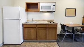 A compact kitchen with a refrigerator, microwave, sink, and a small dining area with a table and chairs. - WoodSpring Suites Washington DC Andrews AFB (Suitland)