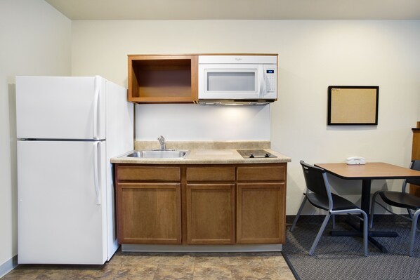 A compact kitchen with a refrigerator, microwave, sink, and a small dining area with a table and chairs. - WoodSpring Suites Washington DC Andrews AFB (Suitland)