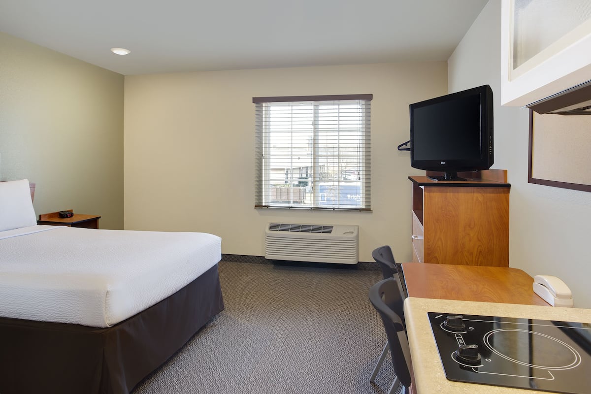 A hotel room with a bed, a desk with a computer, a television, and a window with blinds.
