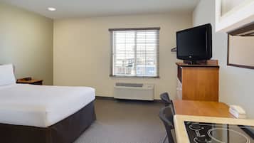 A hotel room with a bed, a desk with a computer, a television, and a window with blinds.