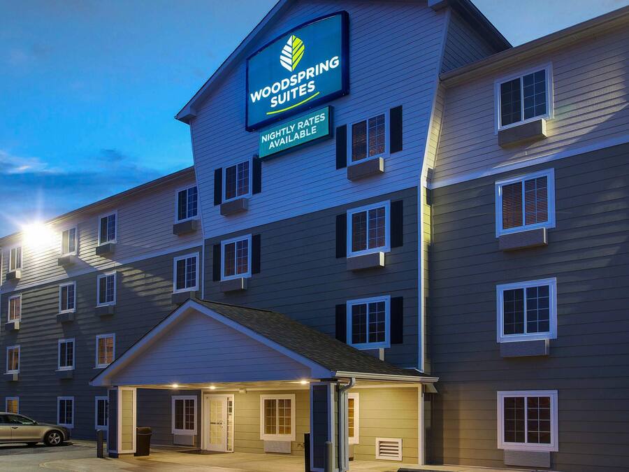 Un hotel de diverses plantes amb un cartell ben visible de WoodSpring Suites que indica disponibilitat.