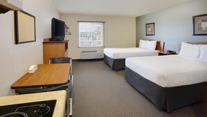 A hotel room with two beds, a desk, a chair, a television, and a window with blinds. - WoodSpring Suites Washington DC Andrews AFB (Suitland)