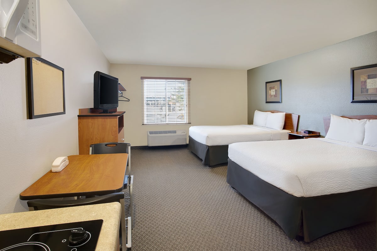 A hotel room with two beds, a desk, a chair, a television, and a window with blinds.