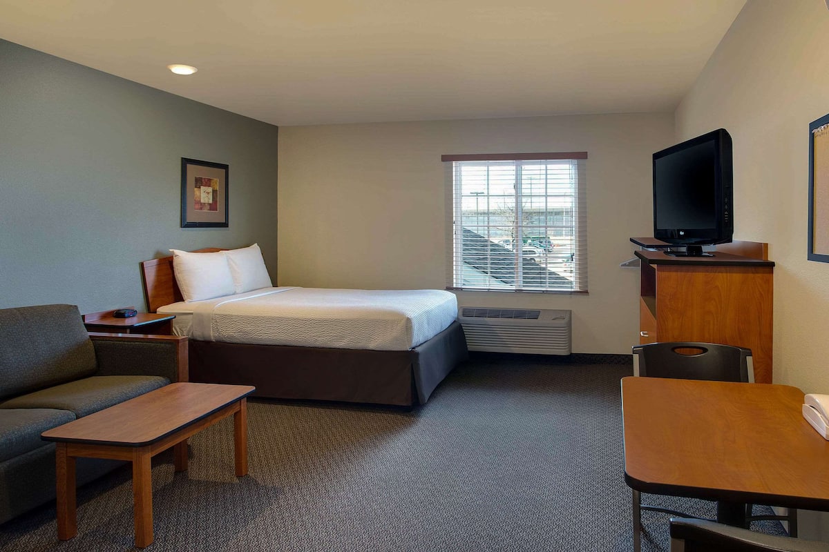 A hotel room with a bed, a sofa, a desk, a television, and a window with blinds.