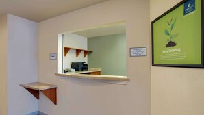 A hotel reception area with a check-in desk, a framed picture of a plant, and a sign indicating check-in and check-out locations. - WoodSpring Suites Washington DC Andrews AFB (Suitland)
