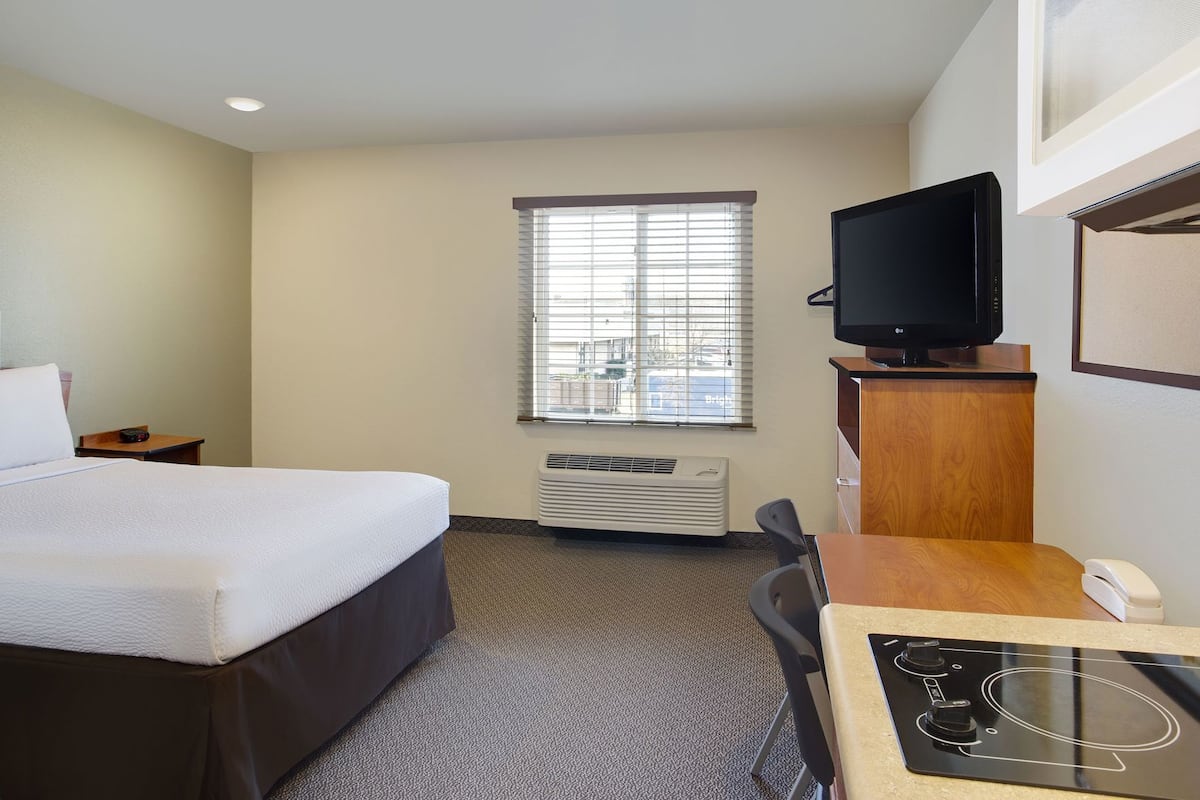A hotel room with a bed, a desk with a telephone, a television, and a window with blinds.