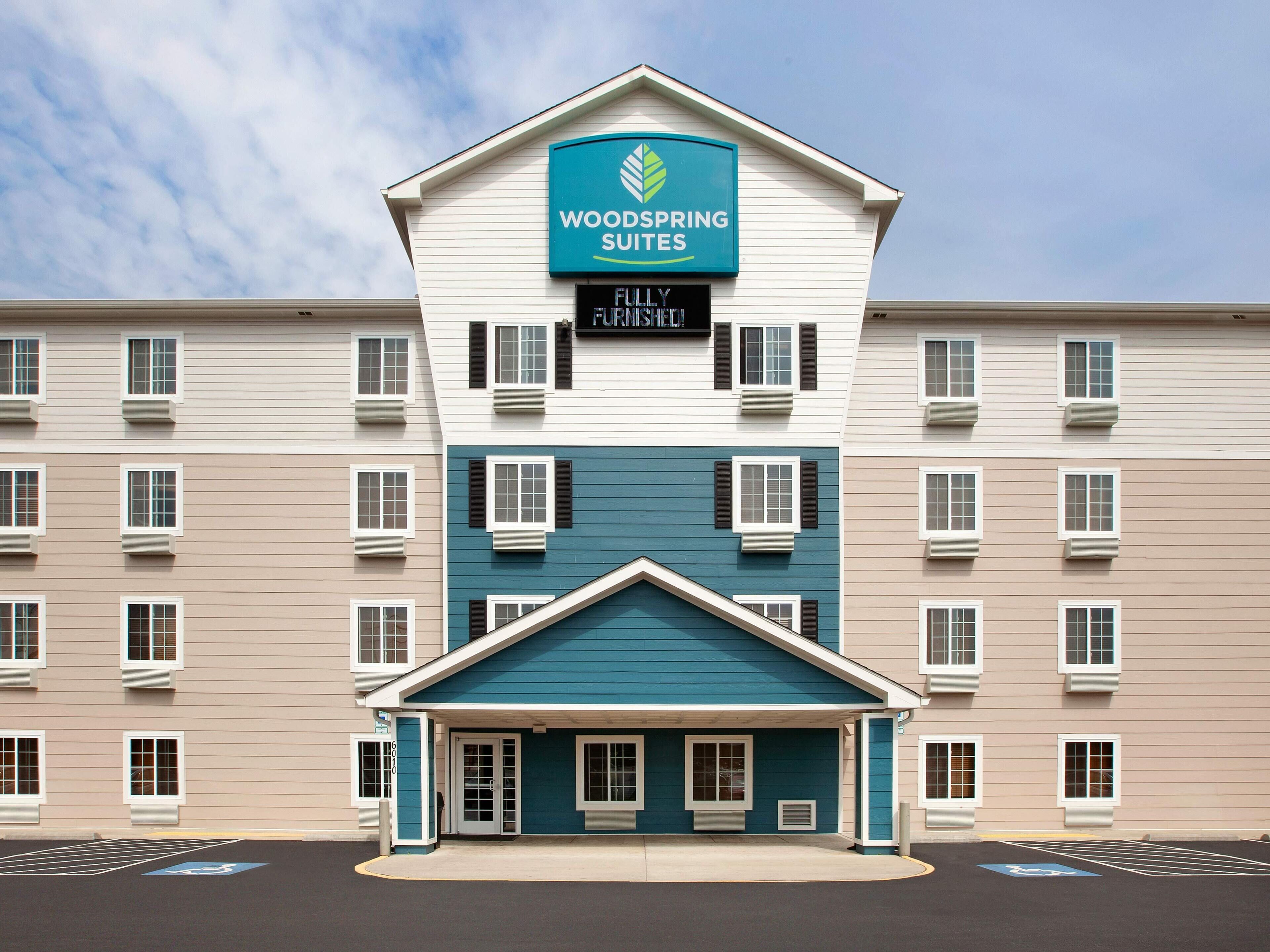 A multi-story hotel with a sign for 'Woodspring Suites' and a 'Fully Furnished' notice.