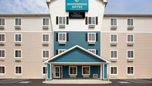 A multi-story hotel with a sign for 'Woodspring Suites' and a 'Fully Furnished' notice. - WoodSpring Suites Washington DC Andrews AFB (Suitland)