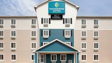 Un hôtel à plusieurs étages, avec une enseigne indiquant « Woodspring Suites » et une affiche précisant « Entièrement meublé ».