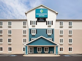Un hotel de varios pisos con un letrero que dice 'Woodspring Suites' y un aviso de 'Completamente amoblado'.