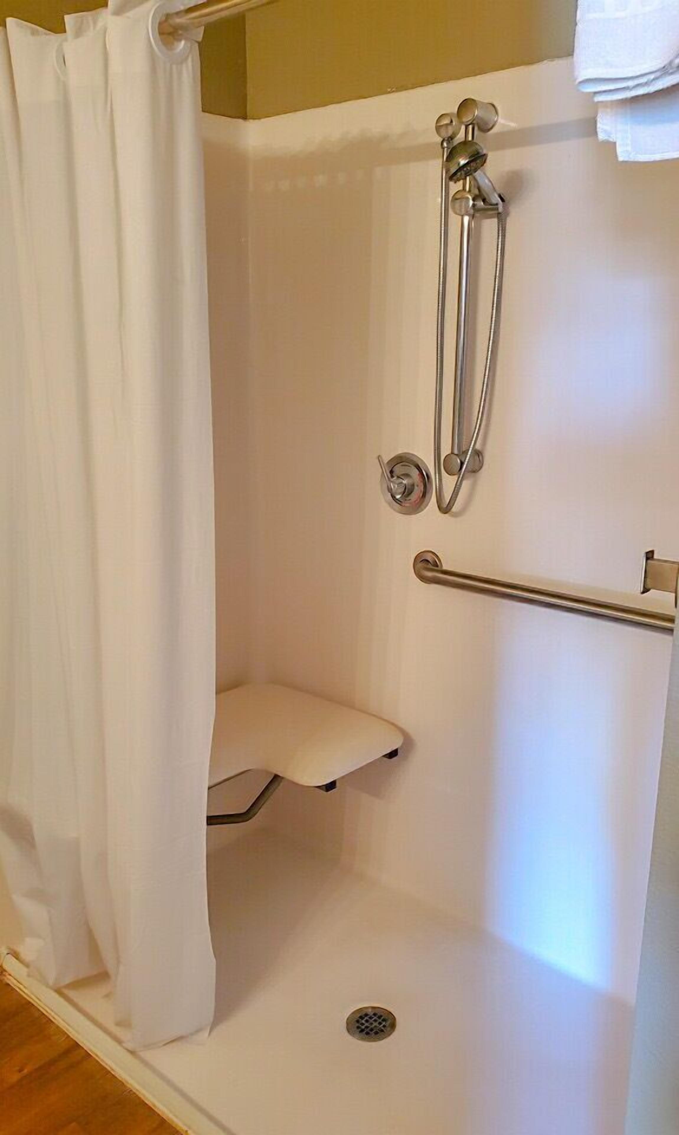 A white shower stall with a grab bar, a small bench, and a showerhead.