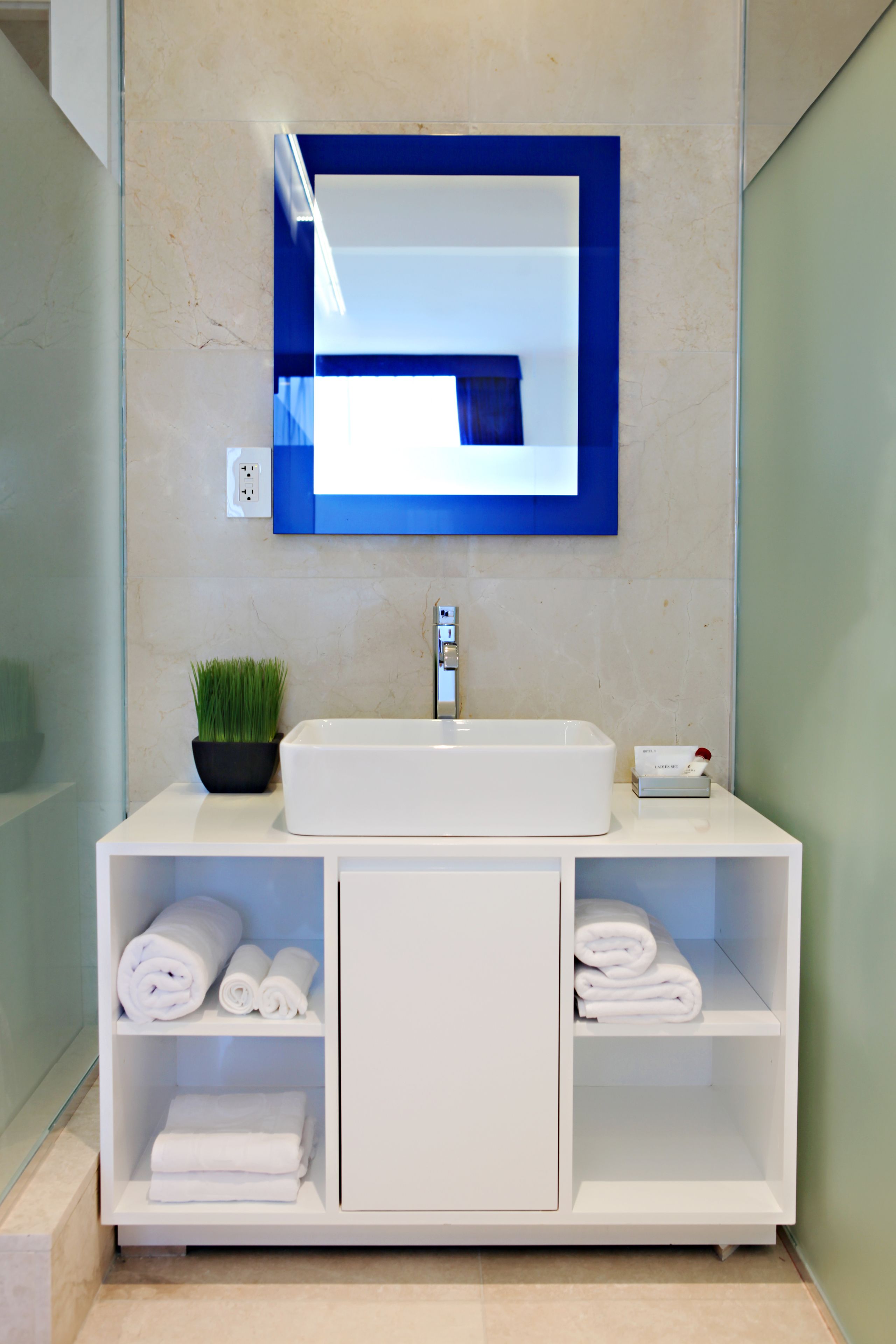 A modern bathroom with a white vanity, a large mirror, and a potted plant.