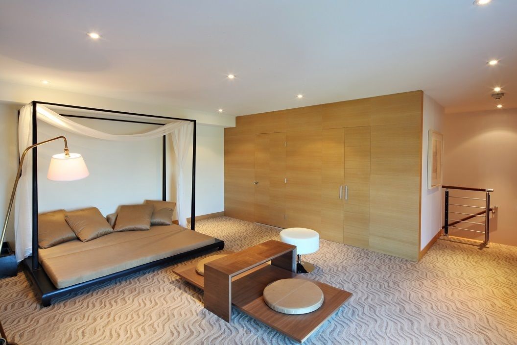 A modern bedroom with a four-poster bed, a bedside table, a wardrobe, and a patterned carpet.