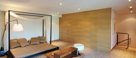 A modern bedroom with a four-poster bed, a bedside table, a wardrobe, and a patterned carpet.
