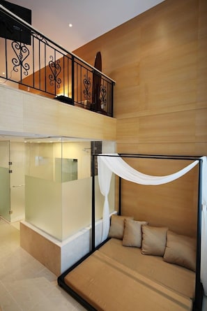 Quarto de hotel moderno com varanda envidraçada, sofá-cama com almofadas bege e parede de madeira.
