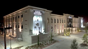 Hotel com uma grande estátua iluminada na fachada, entrada bem iluminada e área ajardinada com árvores.