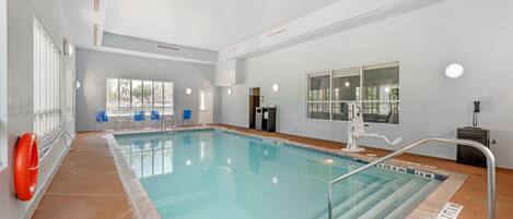 An indoor swimming pool with clear water, a lifebuoy, and a pool ladder.