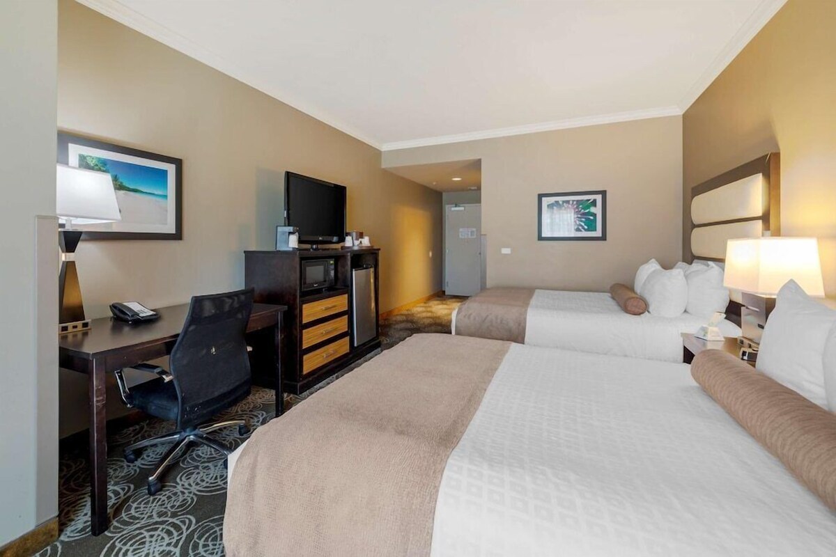 A hotel room with two beds, a desk with a chair, a television, and artwork on the walls.