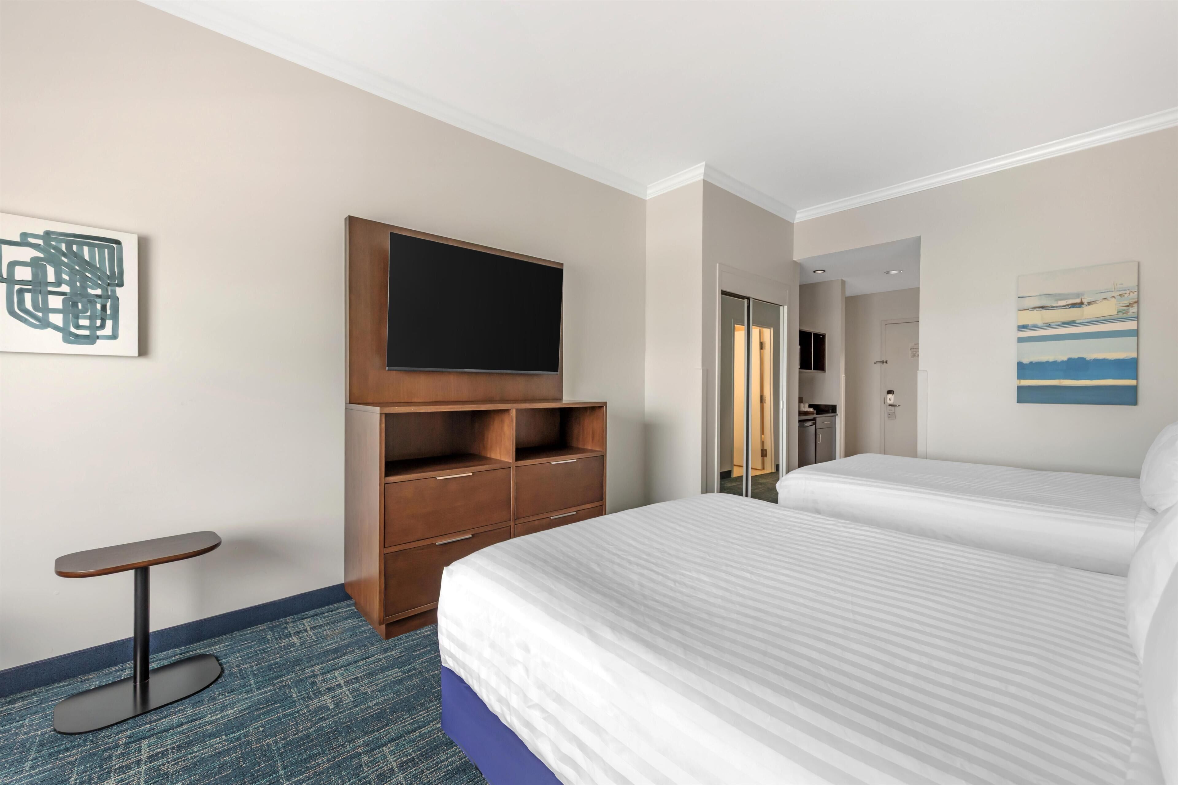 A hotel room with a bed, a TV on a wooden stand, a small table, and a blue carpet.