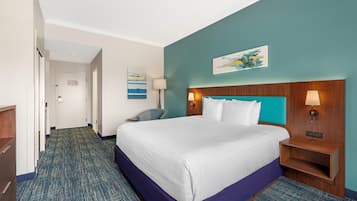 Una habitación de hotel con cama, mesita de noche, lámpara, silla y un cuadro en la pared.