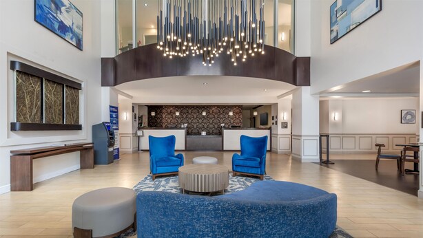 A spacious lobby with a curved blue seating area, a reception desk, and a modern chandelier. - Best Western Plus Miami Airport North Hotel & Suites (Miami Springs)