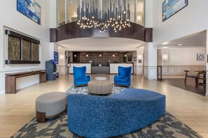 A spacious lobby with a curved blue seating area, a reception desk, and a modern chandelier. - Best Western Plus Miami Airport North Hotel & Suites (Miami Springs)