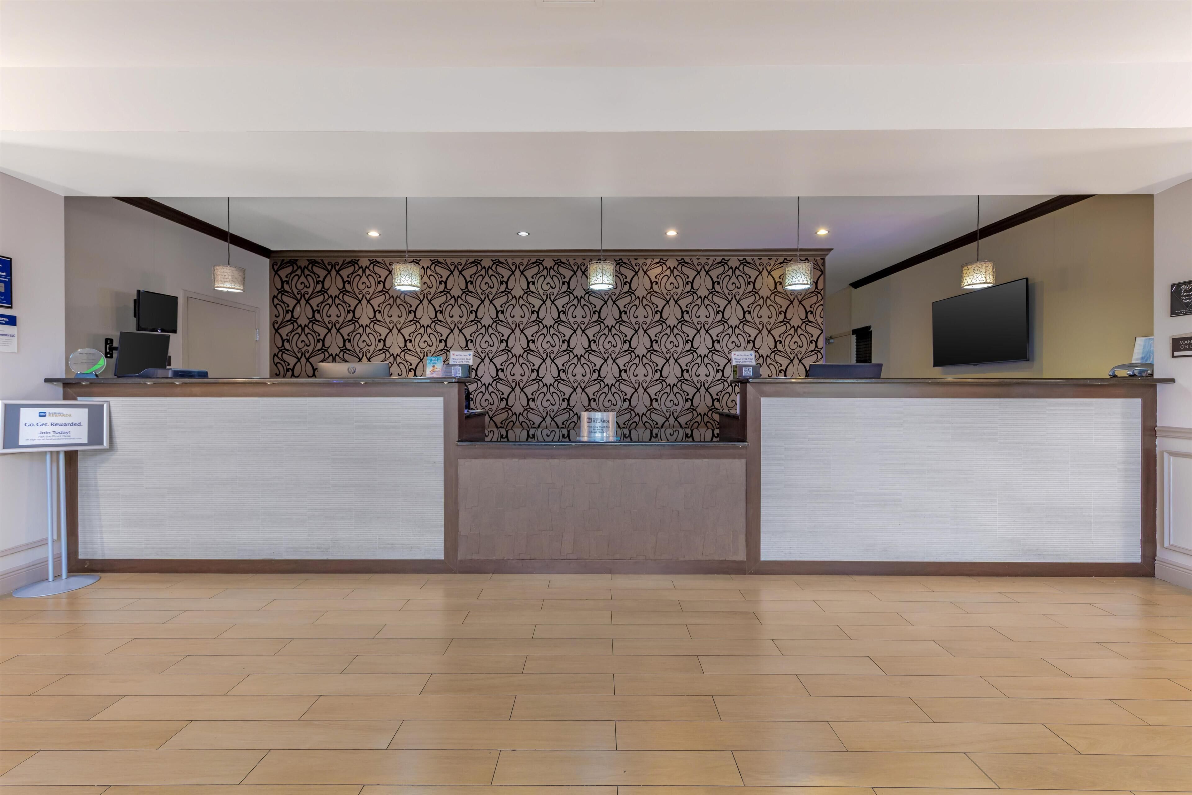 A reception area with a patterned wall, two reception desks, a flat-screen TV, and a sign indicating a co-cab service.