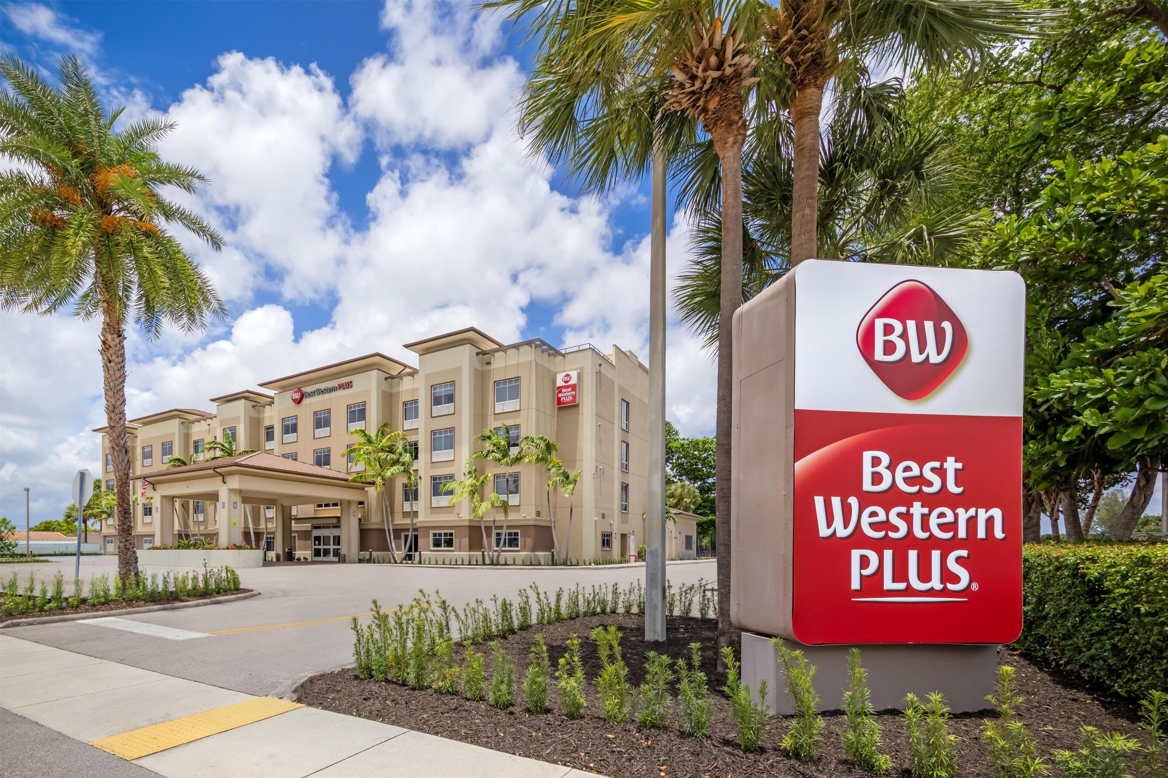 A Best Western Plus hotel with a modern facade, palm trees, and a clear sky.